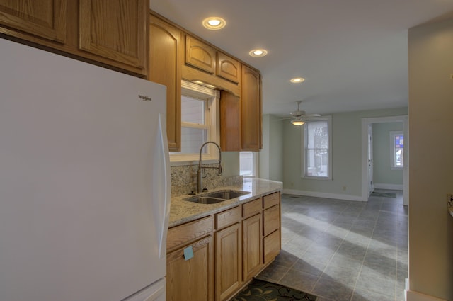 kitchen featuring decorative backsplash, light stone counters, ceiling fan, sink, and white fridge