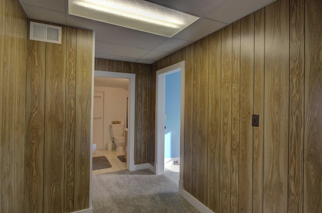 hall with wood walls, a drop ceiling, and light colored carpet