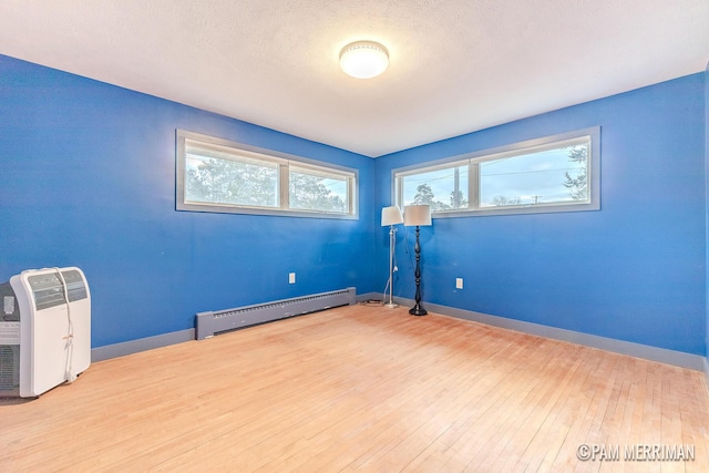 unfurnished room featuring hardwood / wood-style floors, a textured ceiling, and a baseboard heating unit