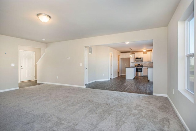 unfurnished living room with visible vents, dark carpet, and baseboards