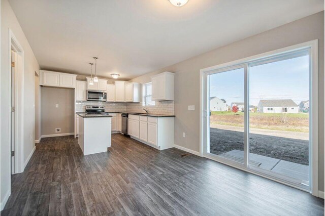 kitchen featuring decorative backsplash, dark countertops, dark wood-style flooring, stainless steel appliances, and white cabinetry