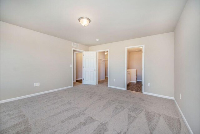 unfurnished bedroom with baseboards, visible vents, a walk in closet, and carpet flooring