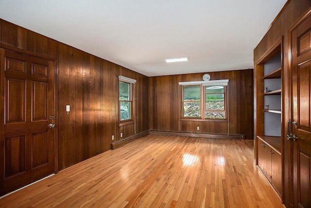 unfurnished room featuring light hardwood / wood-style flooring, a healthy amount of sunlight, and wood walls