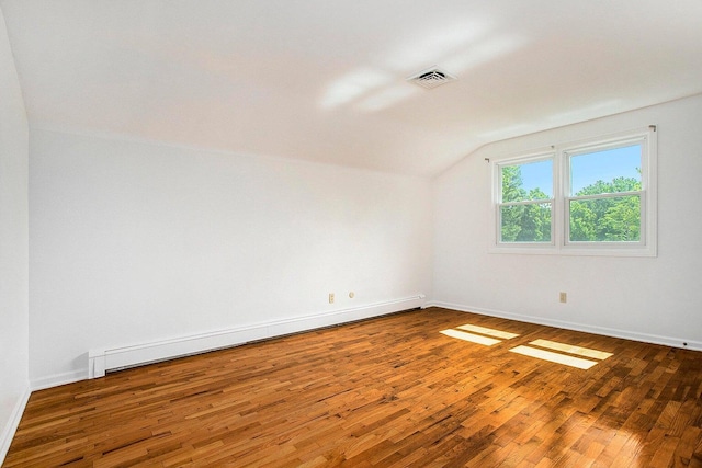 unfurnished room featuring vaulted ceiling, wood-type flooring, and a baseboard heating unit