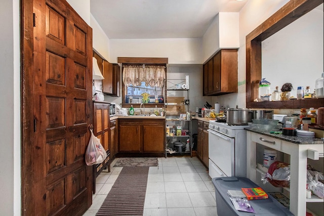 kitchen with white gas stove, light tile patterned floors, and sink