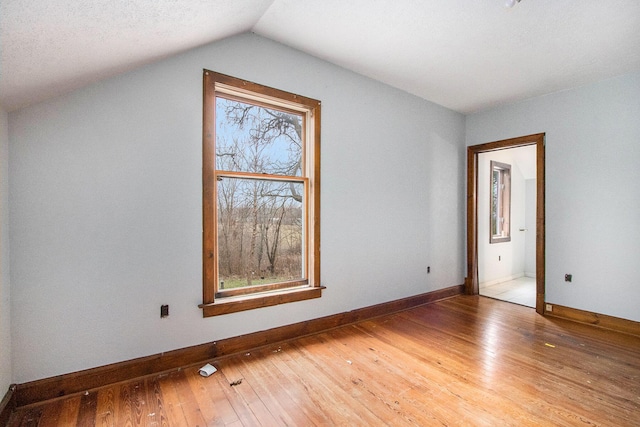 spare room with wood-type flooring, lofted ceiling, and a textured ceiling