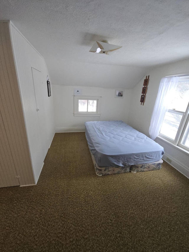 unfurnished bedroom with dark carpet, a textured ceiling, and vaulted ceiling