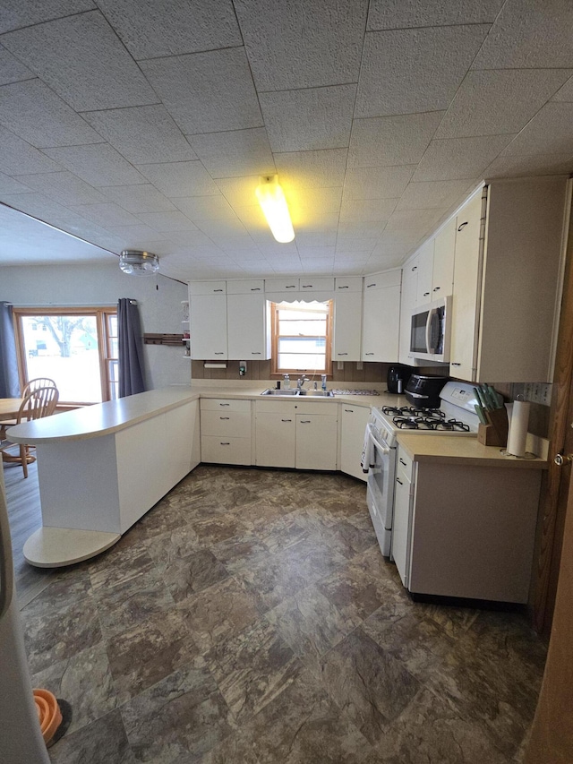 kitchen featuring white range with gas stovetop, kitchen peninsula, white cabinetry, and a wealth of natural light