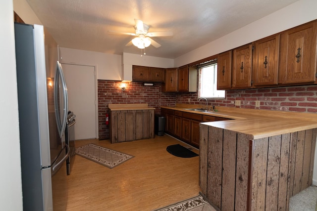 kitchen with brick wall, stainless steel fridge, ceiling fan, and sink