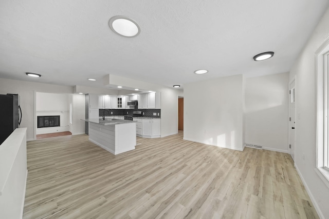 kitchen featuring light hardwood / wood-style flooring, appliances with stainless steel finishes, tasteful backsplash, a kitchen island, and white cabinetry