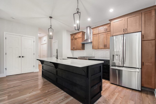 kitchen featuring a center island with sink, a breakfast bar area, wall chimney exhaust hood, light hardwood / wood-style floors, and stainless steel appliances