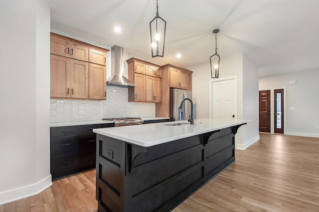 kitchen with a breakfast bar, a kitchen island with sink, wall chimney exhaust hood, light wood-type flooring, and decorative light fixtures