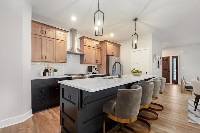 kitchen featuring pendant lighting, a breakfast bar, a kitchen island with sink, wall chimney range hood, and light hardwood / wood-style flooring