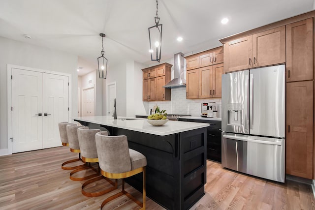 kitchen featuring wall chimney range hood, stainless steel fridge with ice dispenser, light hardwood / wood-style floors, a breakfast bar, and a center island with sink