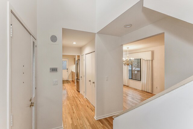 hall featuring recessed lighting, light wood finished floors, baseboards, and a notable chandelier