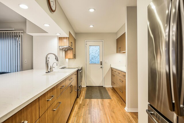 kitchen featuring a sink, brown cabinetry, light wood-style flooring, baseboards, and appliances with stainless steel finishes