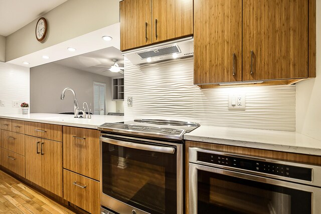 kitchen featuring light wood-style flooring, a sink, range hood, ceiling fan, and appliances with stainless steel finishes