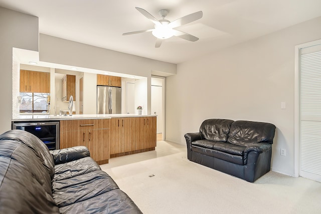 living area featuring beverage cooler, a ceiling fan, baseboards, and light carpet