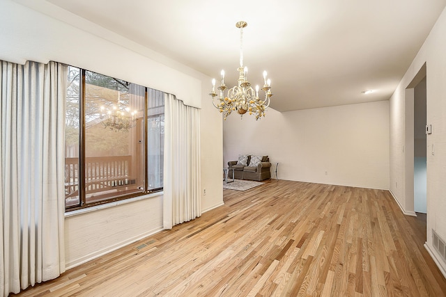 unfurnished room with a notable chandelier, wood finished floors, and visible vents