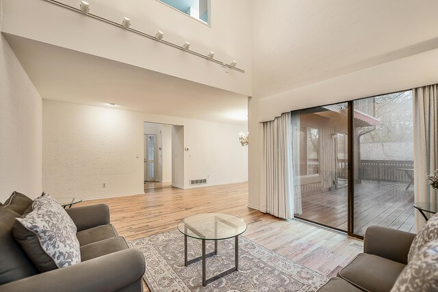 living area featuring a high ceiling, a wealth of natural light, visible vents, and light wood-style flooring