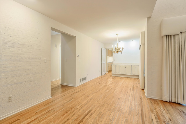 spare room featuring baseboards, light wood-style flooring, visible vents, and a chandelier