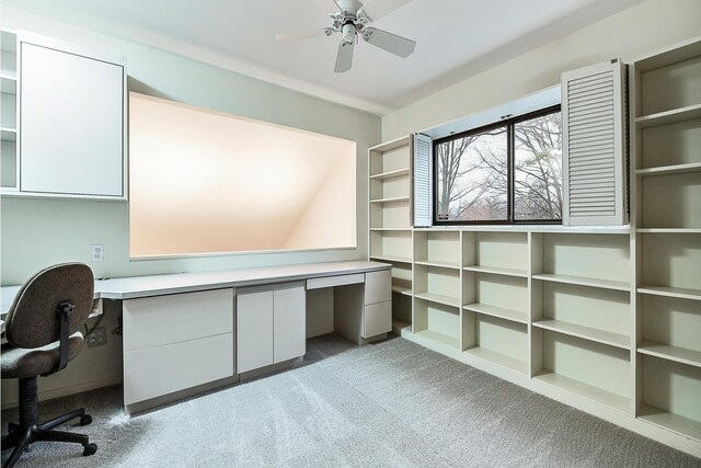 unfurnished office featuring built in desk, light colored carpet, and ceiling fan