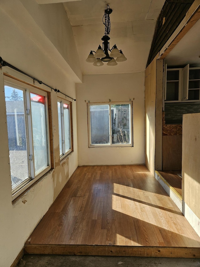 unfurnished room with hardwood / wood-style flooring, an inviting chandelier, and lofted ceiling