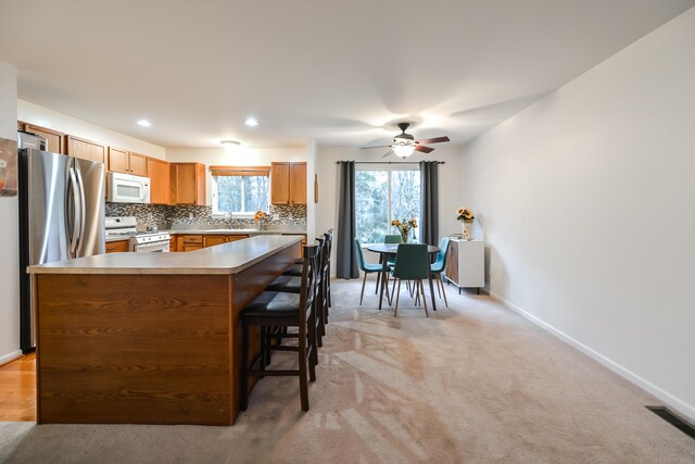 kitchen with light carpet, backsplash, white appliances, ceiling fan, and sink