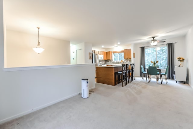 kitchen featuring light carpet, kitchen peninsula, backsplash, ceiling fan, and pendant lighting