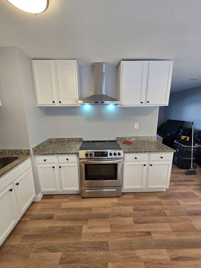 kitchen with wall chimney exhaust hood, white cabinetry, light wood-type flooring, electric stove, and dark stone counters