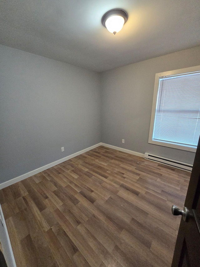 spare room featuring dark wood-type flooring and a baseboard radiator