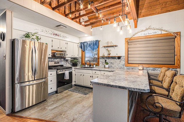 kitchen with stainless steel appliances, kitchen peninsula, a kitchen bar, white cabinets, and light wood-type flooring