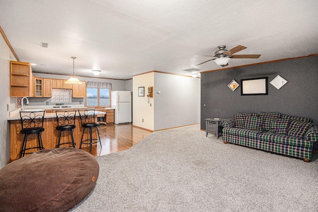 living room with a textured ceiling, light hardwood / wood-style floors, ceiling fan, and crown molding