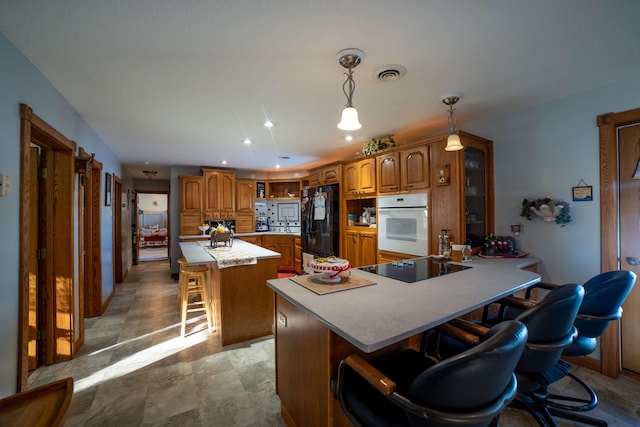 kitchen featuring kitchen peninsula, a breakfast bar, black appliances, pendant lighting, and a kitchen island