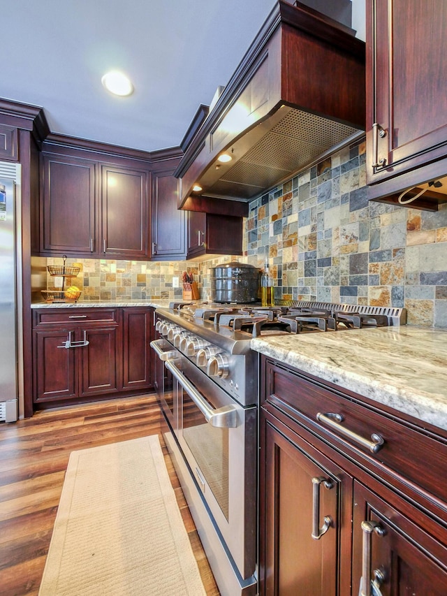 kitchen with decorative backsplash, light wood-type flooring, premium range hood, light stone counters, and high quality appliances