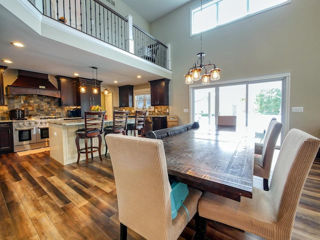 dining space featuring a towering ceiling, dark wood-type flooring, and an inviting chandelier