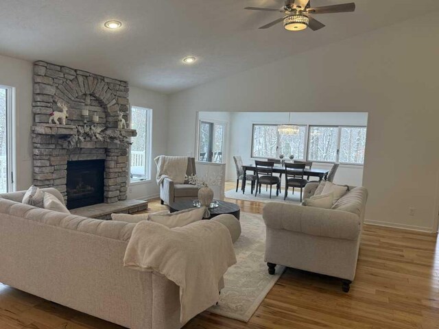 living room with ceiling fan, a stone fireplace, light wood-type flooring, and vaulted ceiling