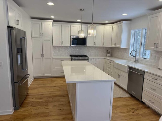 kitchen with white cabinets, appliances with stainless steel finishes, a center island, and decorative light fixtures