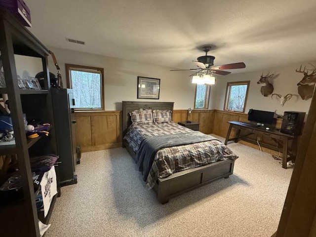 carpeted bedroom featuring ceiling fan, wood walls, and multiple windows