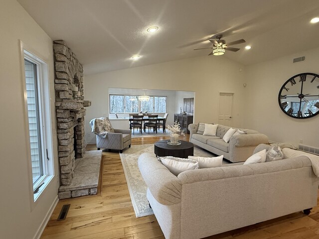 living room with vaulted ceiling, ceiling fan, light wood-type flooring, a fireplace, and a wealth of natural light