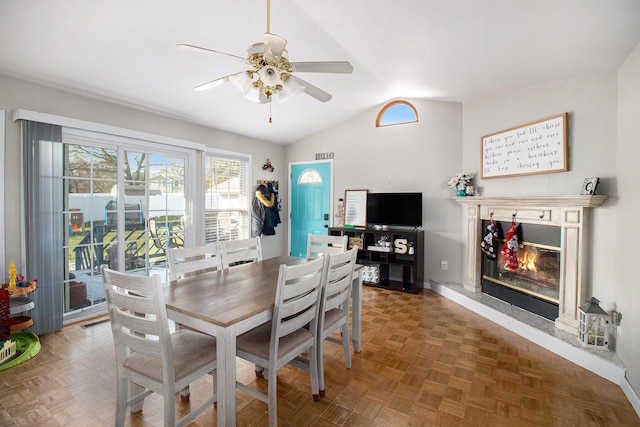 dining area with parquet flooring, vaulted ceiling, ceiling fan, and a premium fireplace