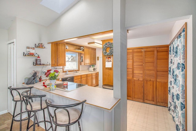 kitchen featuring a kitchen bar, kitchen peninsula, a skylight, electric stovetop, and sink