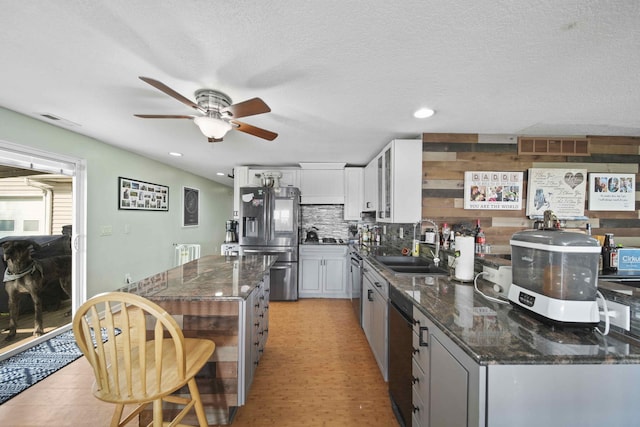 kitchen with ceiling fan, sink, stainless steel appliances, dark stone counters, and white cabinets