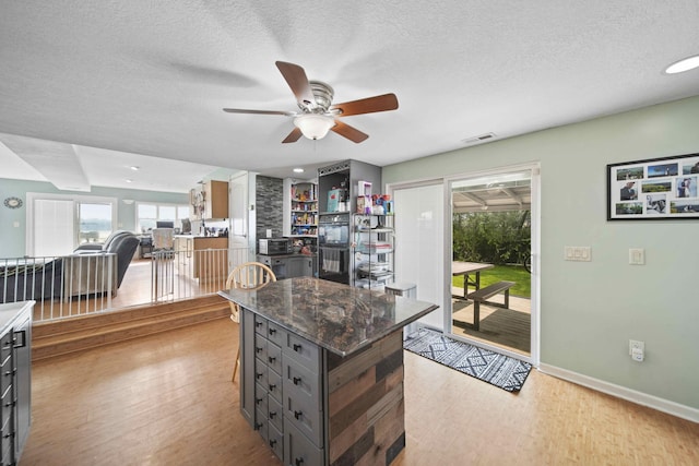 kitchen with a textured ceiling, light wood-type flooring, a center island, and ceiling fan