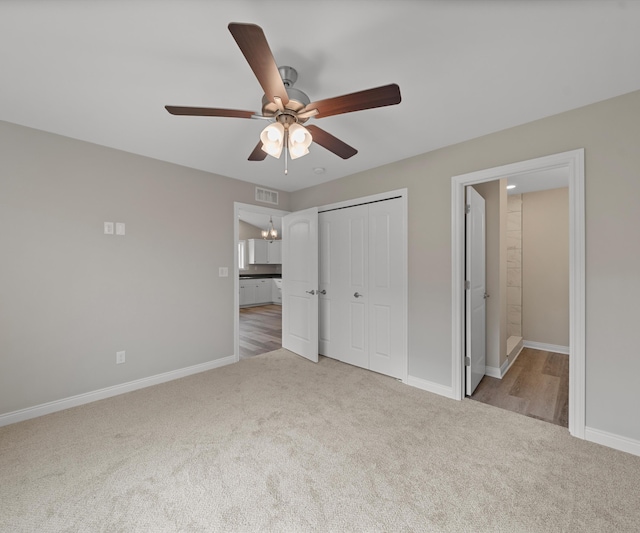 unfurnished bedroom featuring ceiling fan, a closet, light colored carpet, and ensuite bath