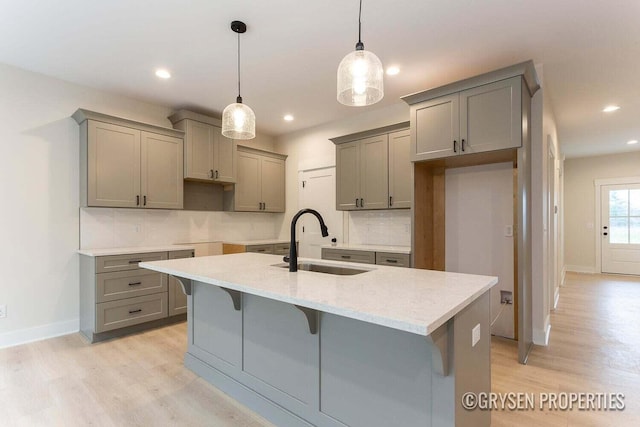 kitchen featuring sink, hanging light fixtures, tasteful backsplash, an island with sink, and light hardwood / wood-style floors