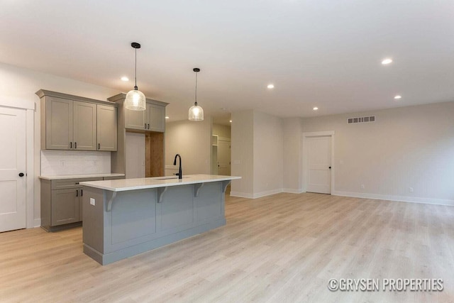 kitchen with gray cabinetry, sink, decorative light fixtures, a center island with sink, and light hardwood / wood-style floors