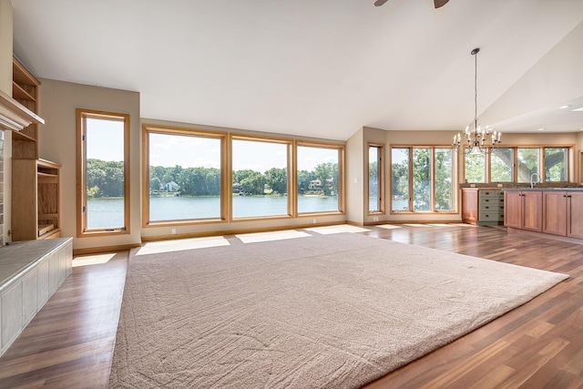 unfurnished living room featuring sink, wood-type flooring, lofted ceiling, a water view, and ceiling fan with notable chandelier