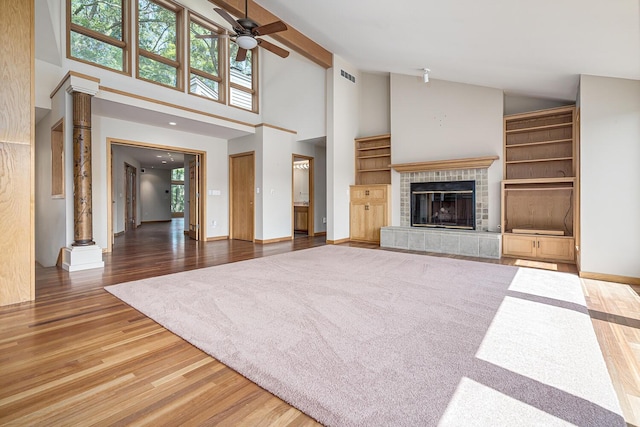 unfurnished living room featuring dark hardwood / wood-style flooring, ceiling fan, high vaulted ceiling, beamed ceiling, and a tiled fireplace