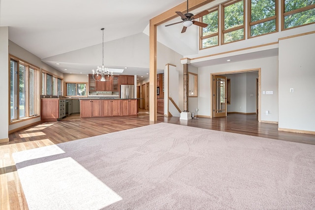 unfurnished living room featuring ceiling fan with notable chandelier, sink, dark wood-type flooring, and high vaulted ceiling